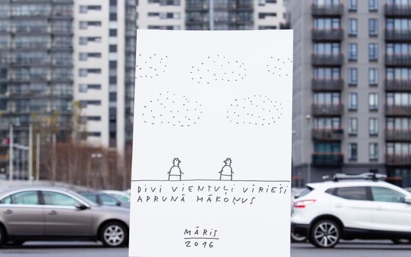 Liels, ar roku zīmēts plakāts uz molberta attēlo divas figūras zem punktētiem mākoņiem ar tekstu "Divi vientuļi vīrieši aprunā mākoņus" apakšā. Plakāts novietots ārā uz augstu, modernu ēku fona.