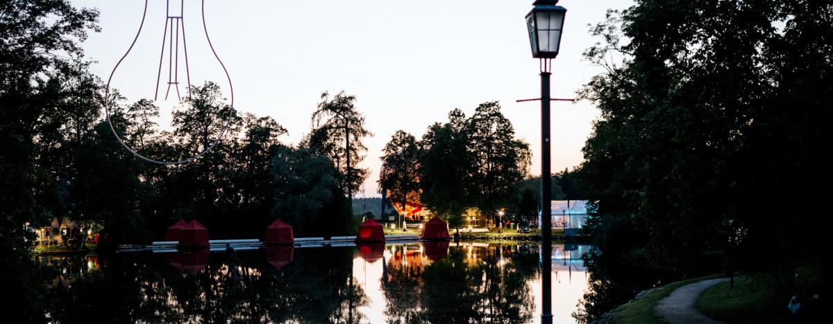 Krēslas stunda redzams Cēsu Pils parka dīķis ar skatuvi uz ūdens un festivāla dekorācijām