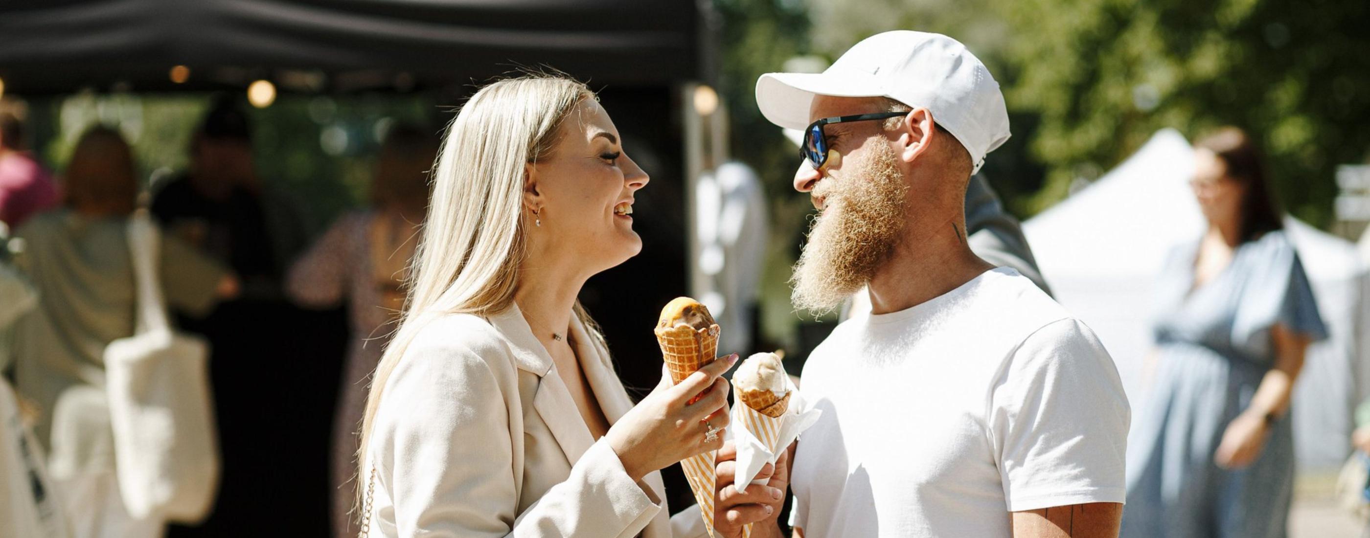 jauna sieviete un jauns vīrtietis baltās drēbēs ēd saldējumu