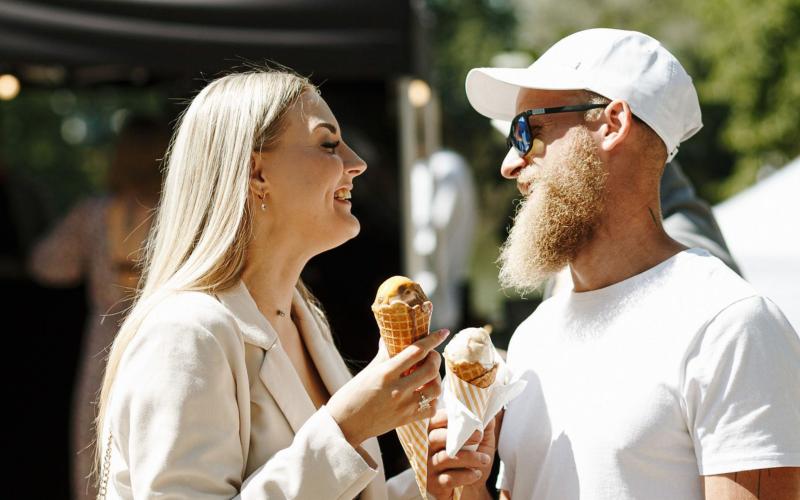 jauna sieviete un jauns vīrtietis baltās drēbēs ēd saldējumu