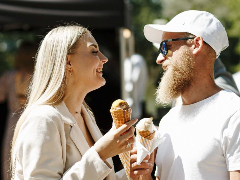 jauna sieviete un jauns vīrtietis baltās drēbēs ēd saldējumu